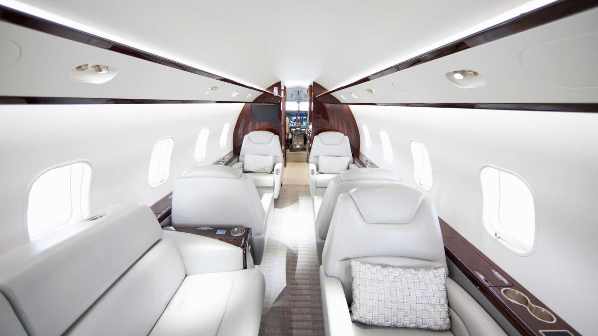 Interior de cabina de jet privado de lujo con asientos en piel blanca y acabados en madera, configurada para vuelo chárter.